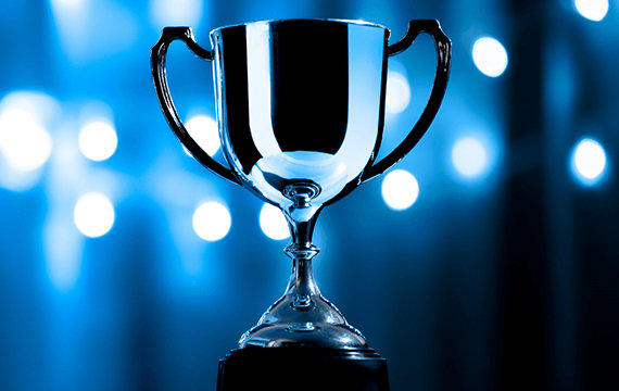A shiny silver trophy cup with handles on both sides, set against a blue background with blurred lights.